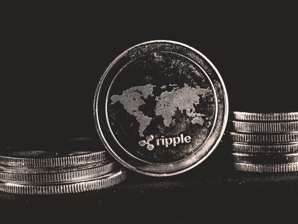 Black-and-white Ripple coin on stacked coins representing XRP price and XRP trading activity, with XRP futures volume and the XRPL Ledger Batch upgrade under XRPL validator support