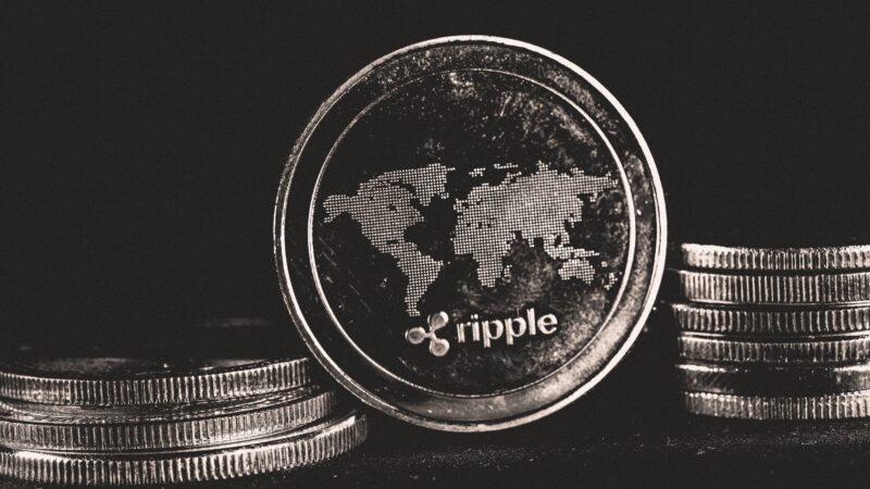 Black-and-white Ripple coin on stacked coins representing XRP price and XRP trading activity, with XRP futures volume and the XRPL Ledger Batch upgrade under XRPL validator support